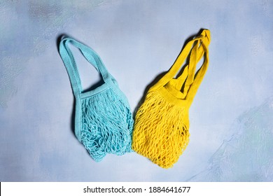 Two Empty Yellow And Blue Mesh Bags On Blue Textured Concrete Background. Flat Lay. Horizontal Orientation. Conscious Consumerism And Eco Friendly Shopping Concept.