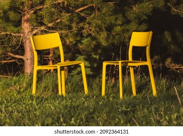 Two Empty Yellow Chairs Facing Each Other In A Forest On A Warm Summer Evening