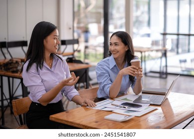 Two engaging Asian businesswomen having a lively discussion during a coffee break in a casual office setting.

 - Powered by Shutterstock