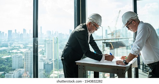 Two Engineer or Architect are analyzing blueprints while working on a new project on construction site with blue sky and city background.Architect supervising construction on terrace tower.