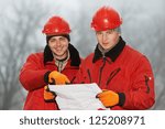 Two engineer builders with blueprint plan at construction site