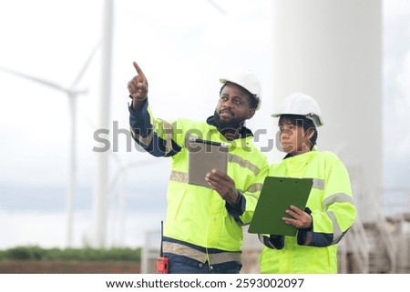 Two engineer check and examining wind turbines in wind farm, renewable energy and teamwork in a sustainable environment, inspection power electric with document and tablet, industry and eco.