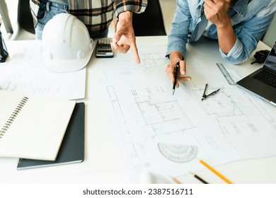 Two engineer working to discuss and collaborate about blueprint of construction project in office.
