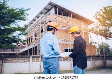 Two engineering man with helmet and paper work are discussing about the project over construction site background. 