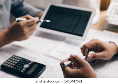 Two engineering working together and using digital tablet looking blueprint and analysis with architectural plan on desk.