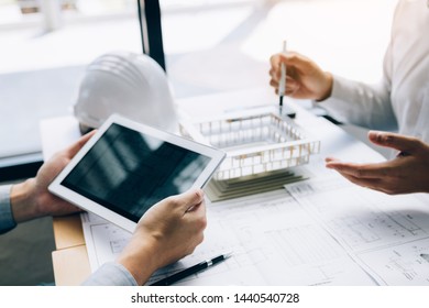 Two engineering working together and using digital tablet looking blueprint and analysis with architectural plan on desk.