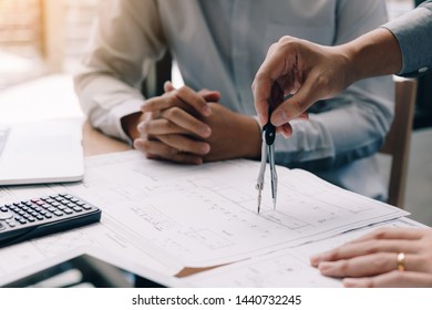 Two engineering working together and using digital tablet looking blueprint and analysis with architectural plan on desk.