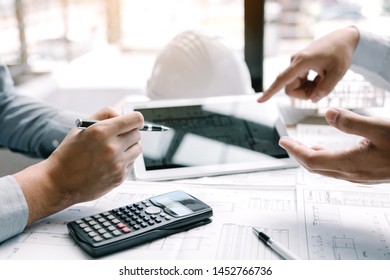Two engineering working together and using digital tablet looking blueprint and analysis with architectural plan on desk.