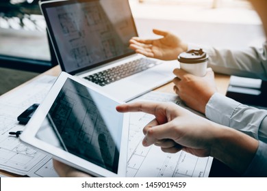 Two engineering working together and using digital tablet looking blueprint and analysis with architectural plan on desk.