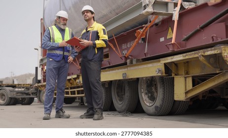 Two engineers collaborate on quality control, inspecting a heavy cargo shipment at an industrial site to manage supply chain logistics and ensure compliance.