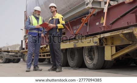 Two engineers collaborate on quality control, inspecting a heavy cargo shipment at an industrial site to manage supply chain logistics and ensure compliance.