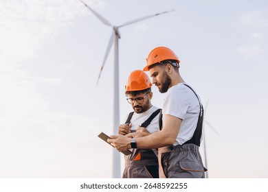 Two engineers collaborating on a tablet, focusing on the maintenance and innovation of a wind turbine for sustainable energy production