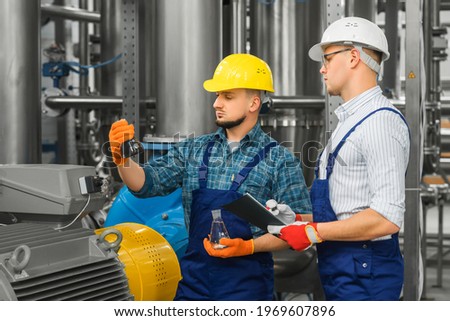 Two engineers consider the results of purification of dirty industrial water. Wastewater treatment plants on the background. Workers compare flasks with dirty and purified water.