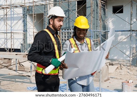 Two engineers discussing architectural plans on active construction site with scaffolding, focused teamwork and safety management concept, eye level view with realistic lighting and authentic work atmosphere.