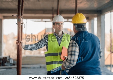 Two engineers discussing building progress at a construction site, reviewing plans and collaborating on project development and design