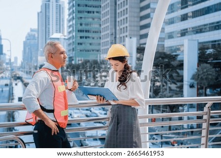 Two engineers discussing a construction project with a clipboard on a skywalk in a modern city. Wearing safety gear, they represent teamwork, planning, urban development, and on-site collaboration.