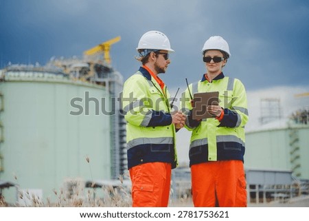 Two engineers discussing task progress and reviewing checklist at gas refinery site