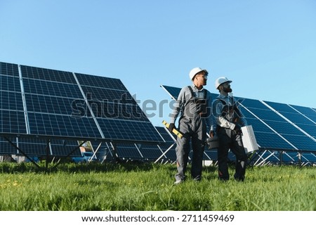 Two engineers holding tools and installing solar panels in a green field with a clear blue sky, representing renewable energy and sustainability