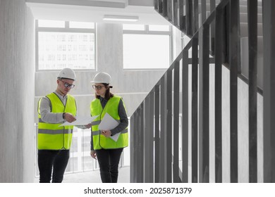 Two Engineers, A Man And A Woman In White Helmets And Green Protective Vests, Work At The Construction Site, Professional And Licensed Engineers In Construction And Fire Safety Technology Take