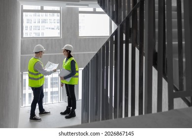 Two Engineers, A Man And A Woman In White Helmets And Green Protective Vests, Work At The Construction Site, Professional And Licensed Engineers In Construction And Fire Safety Technology Take