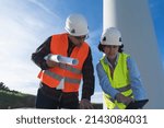 Two engineers with protective clothes using digital tablet and working on a windmill farm.
