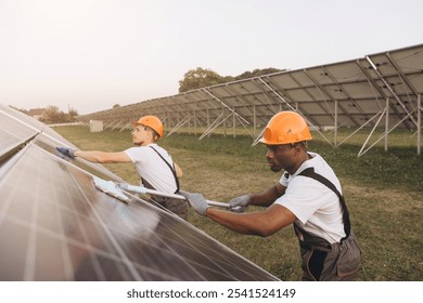 Two engineers in protective gear cleaning solar panels in a field, promoting renewable energy and sustainability. They demonstrate teamwork and environmental awareness in the clean energy sector. - Powered by Shutterstock