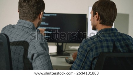 Two engineers review and debug code together on a monitor in a modern office. A teamwork-driven moment in a real-world development and problem-solving environment.