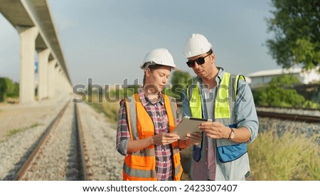 Two engineers in safety uniform and helmet using tablet discussion and inspection construction process railway while walking. Two engineer working on railway together. Teamwork concept