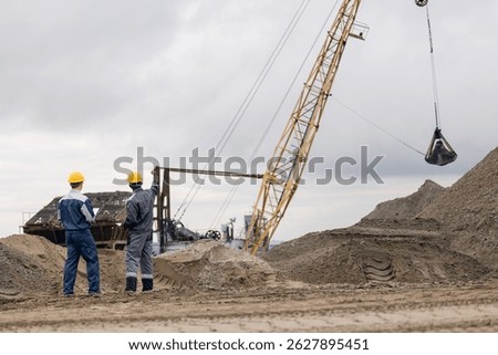 Two Engineers at sand quarry mining site with heavy machinery, back view.