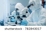 Two Engineers/ Scientists/ Technicians in Sterile Cleanroom Suits Use Microscopes for Component Adjustment and Research. They Work in an Electronic Components Manufacturing Factory.