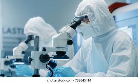 Two Engineers/ Scientists/ Technicians In Sterile Cleanroom Suits  Control Manufacturing Machinery Work And Use Microscopes For Component Adjustment And Research. They Work In An Manufactory.