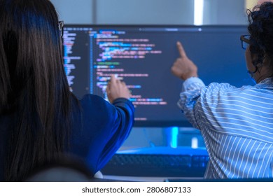 Two engineers seen from behind studying source code on large monitors facing a wall of monitors filled with source code. The candid moment captures modern software development, modernoffice.