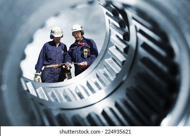 two engineers seen through a large cogwheels gear shaft, metal industry