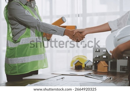 Two engineers shaking hands after concluding a successful meeting in the office, with blueprints and scale models on the table