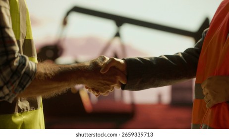 Two engineers shaking hands in front of a pump jack at an oil extraction site, celebrating successful cooperation