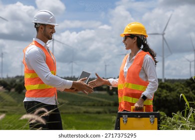 Two engineers shaking hands at wind farm site, wearing safety helmets and vests, symbolizing successful collaboration and renewable energy project teamwork.
