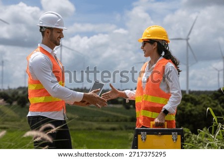 Two engineers shaking hands at wind farm site, wearing safety helmets and vests, symbolizing successful collaboration and renewable energy project teamwork.