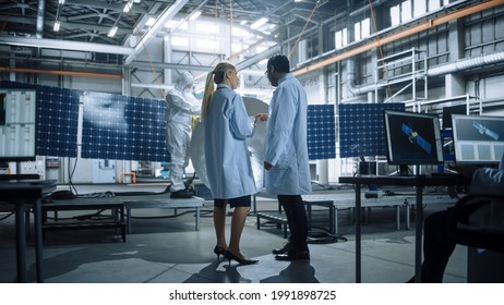Two Engineers Talk, Use Tablet Computer while Working on Satellite Construction. Aerospace Agency Manufacturing Facility: Scientists Build, Assemble Spacecraft for Space Exploration Mission