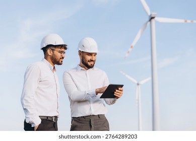 Two engineers using a digital tablet are checking data about sustainable energy production in a wind turbine power plant