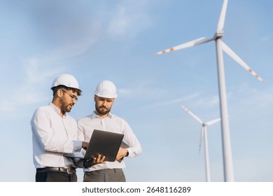 Two engineers using a laptop are analyzing the operation of wind turbines in a wind farm, promoting sustainable energy and environmental protection