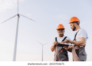 Two engineers using a tablet and inspecting wind turbines in a wind farm, renewable energy and eco friendly industry