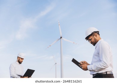 Two engineers using technological devices working in a wind turbine power plant for sustainable energy production