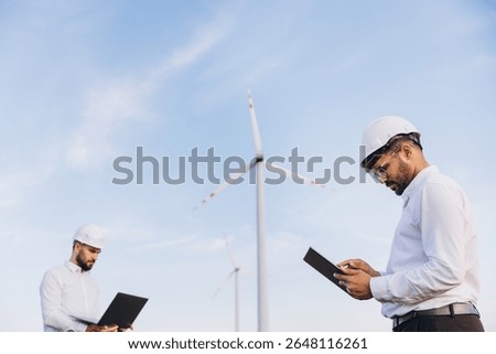 Two engineers using technological devices working in a wind turbine power plant for sustainable energy production