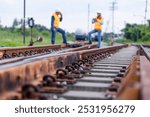 Two engineers wearing safety gear and clothing inspect the tracks of a natural gas transport train. Focus on the railroad spikes.Rail Maintenance, Logistics, and Industrial Transportation