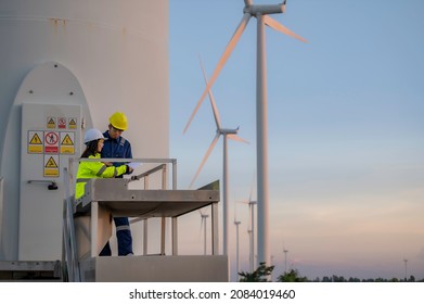 Two Engineers Working And Holding The Report At Wind Turbine Farm Power Generator Station On Mountain,Thailand People,Technician Man And Woman Discuss About Work