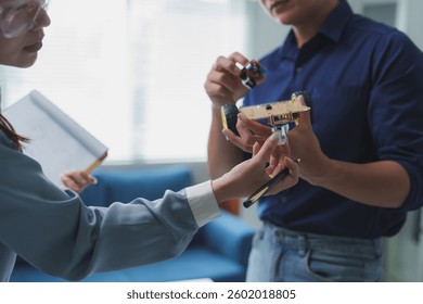 Two engineers are working together, assembling and examining a robot prototype, discussing design and functionality in a brightly lit, modern office environment