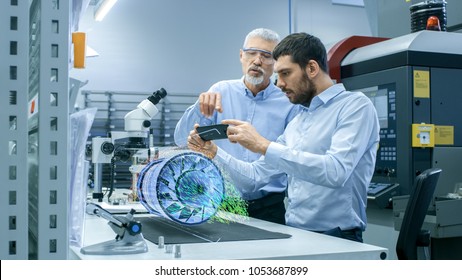 Two Engineers Works With Mobile Phone Using Augmented Reality Holographic Projection 3D Model Of The Engine Turbine Prototype. Development Of Virtual Mixed Reality Application.