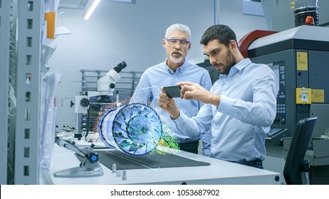 Two Engineers Works with Mobile Phone Using Augmented Reality Holographic Projection 3D Model of the Engine Turbine Prototype. Development of Virtual Mixed Reality Application. - Shutterstock ID 1053687902