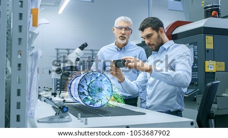 Two Engineers Works with Mobile Phone Using Augmented Reality Holographic Projection 3D Model of the Engine Turbine Prototype. Development of Virtual Mixed Reality Application. Stockfoto © 