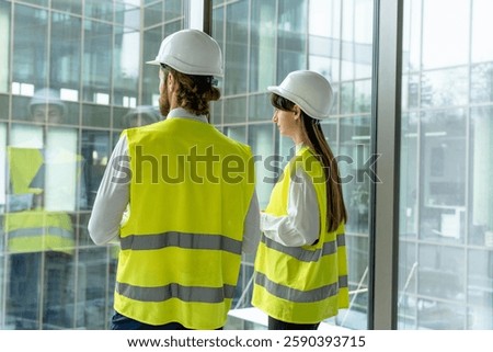 Two engineers in yellow vests standing at the panoramic window